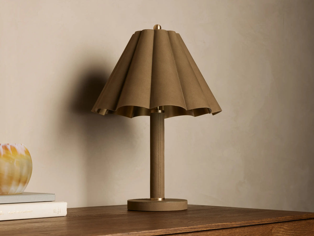 Lucy Accent Table Lamp features a pleated tan leather shade and cylindrical base, sitting on a wooden table next to books and a vase.
