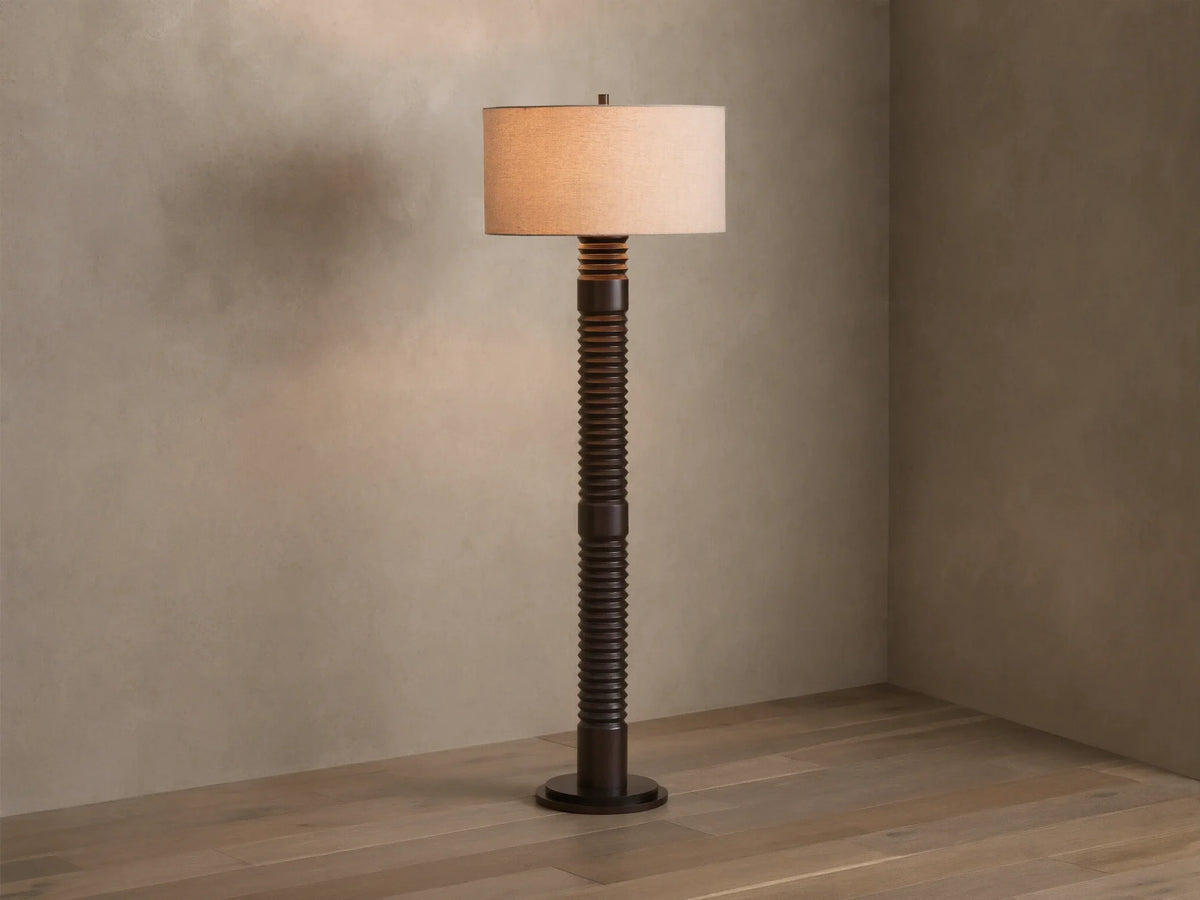 Front view of a dark brown ribbed floor lamp with a cylindrical beige fabric shade, emitting a warm glow.