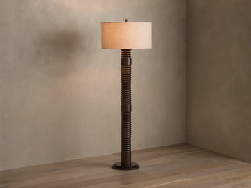 Front view of a dark brown ribbed floor lamp with a cylindrical beige fabric shade, emitting a warm glow.