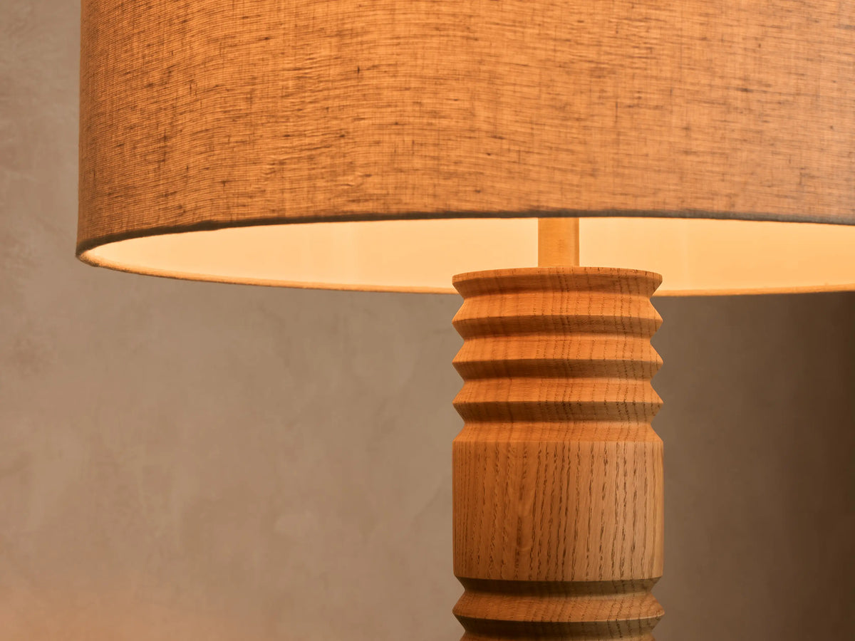 Front view of a tall floor lamp with a beige fabric drum shade and a natural wood base with a ribbed column stem.