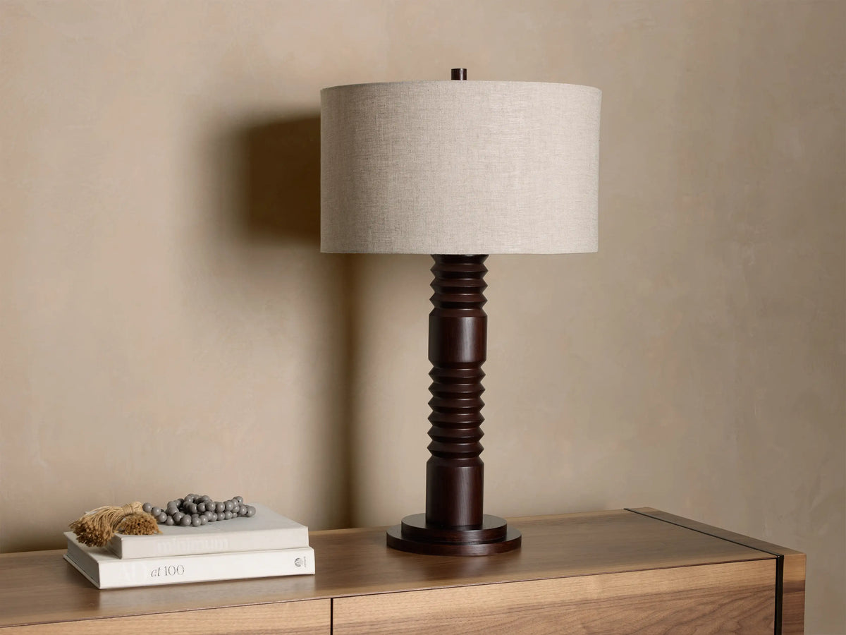 Front view of a dark brown carved wood table lamp with a light beige linen cylindrical shade.