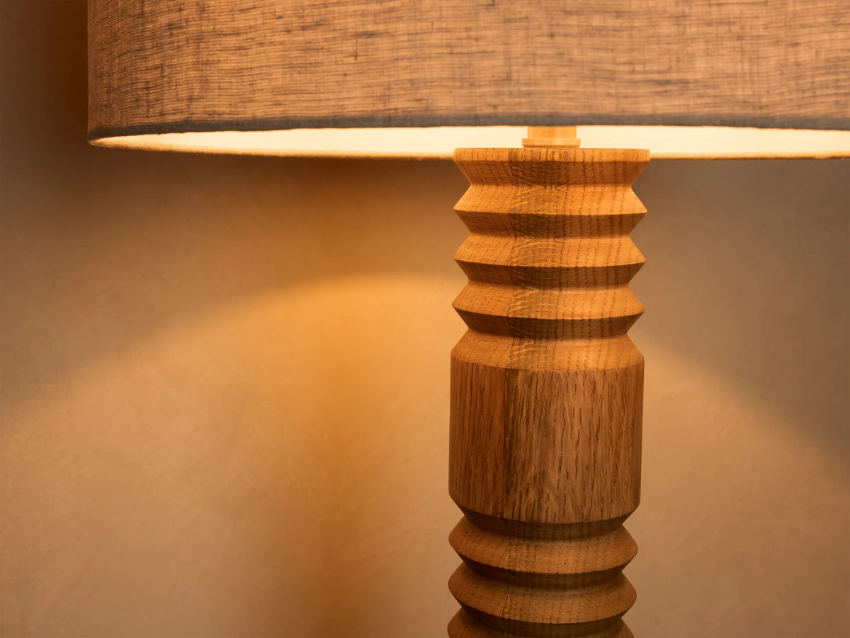 Close-up of a table lamp with a light brown carved wooden base and a textured gray fabric shade emitting warm light.
