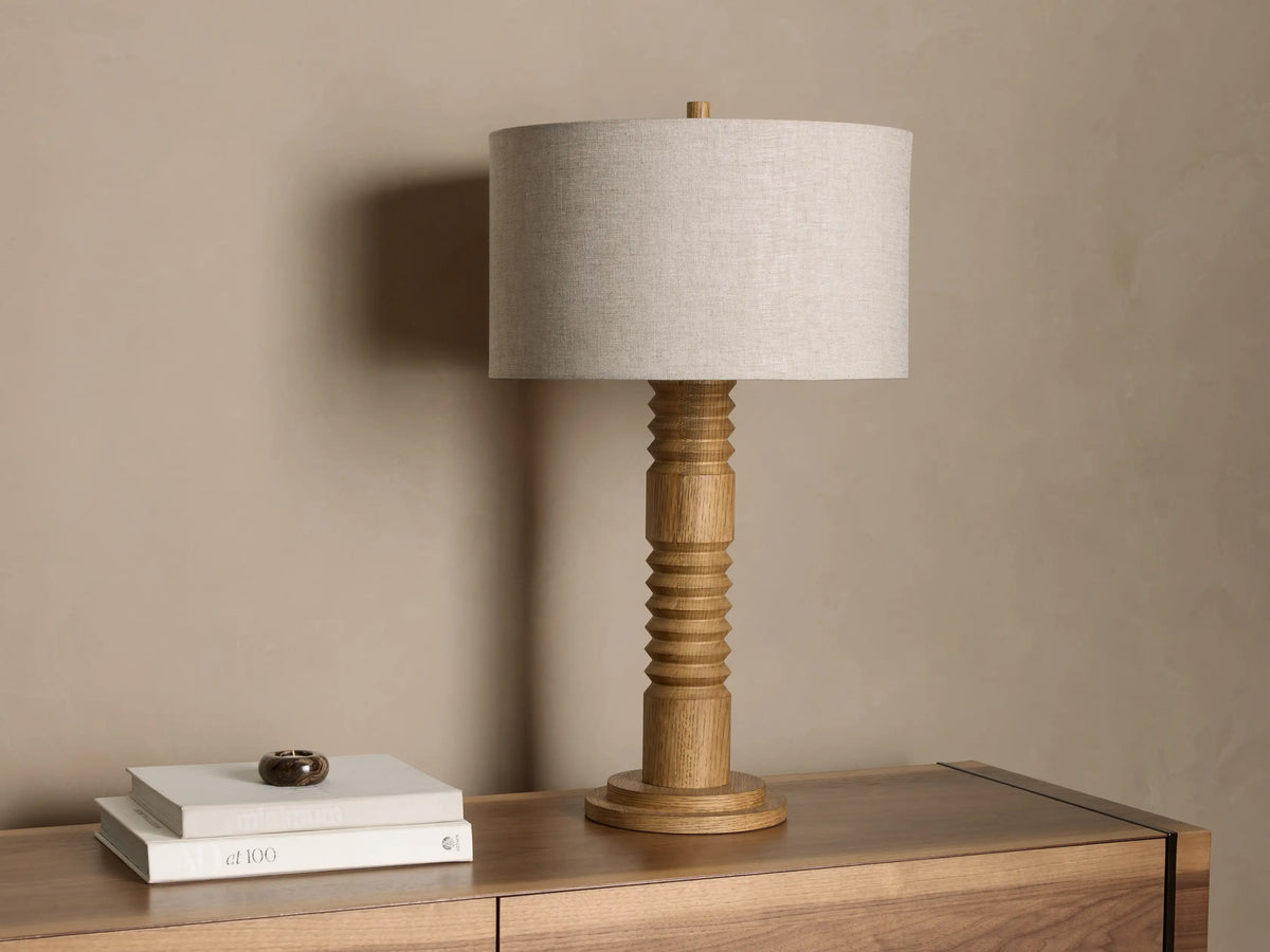 Front view of an illuminated natural wood Fluted Table Lamp with a light beige fabric cylindrical shade.