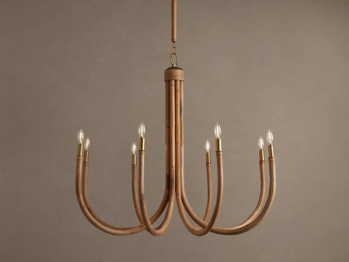Ravda Round Chandelier features 8 curved rattan arms with brass details, holding glowing clear bulbs, hanging against a brown wall.