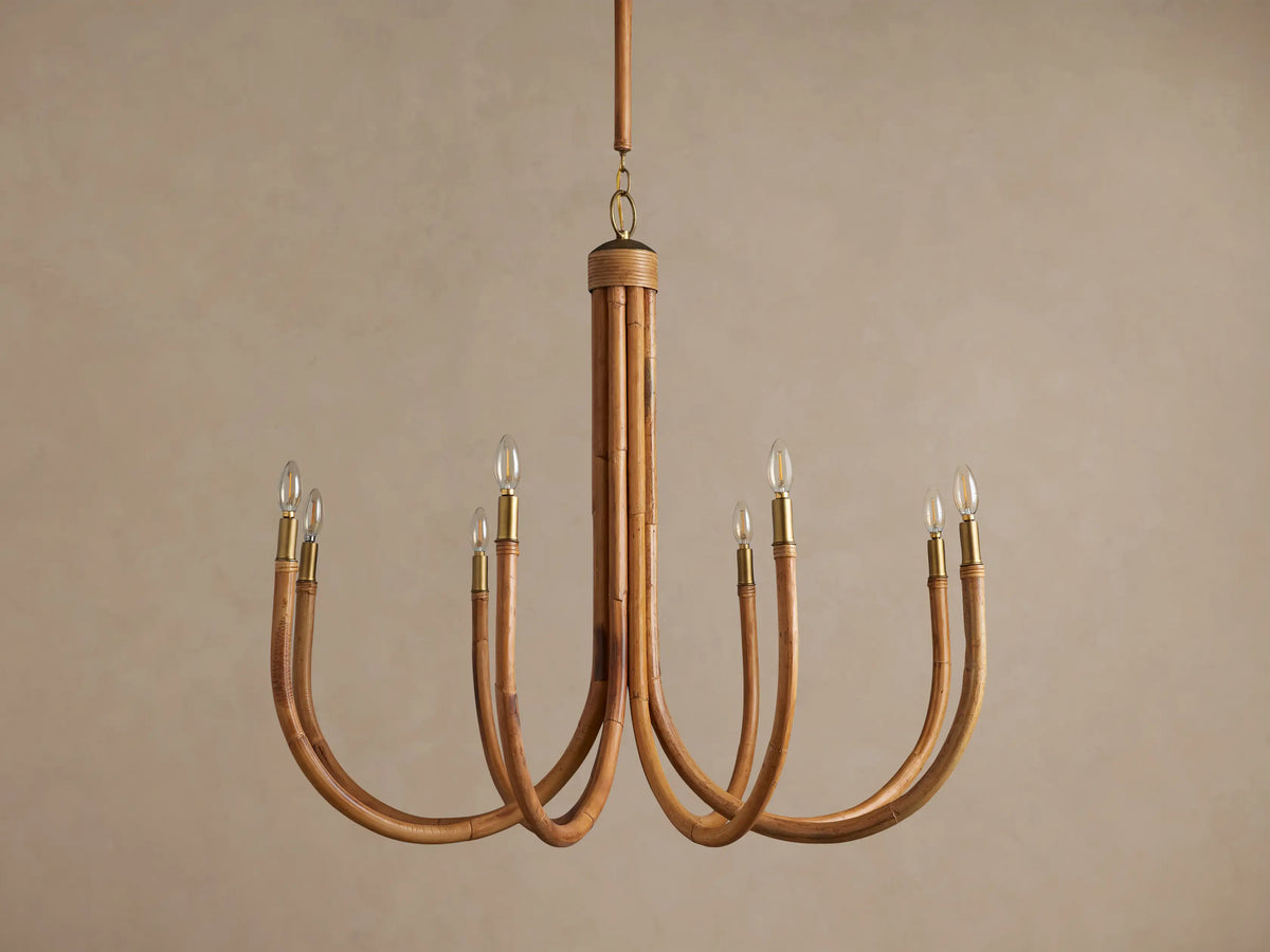 Ravda Round Chandelier made of natural light brown rattan with eight curved arms, brass details, and candelabra bulbs.