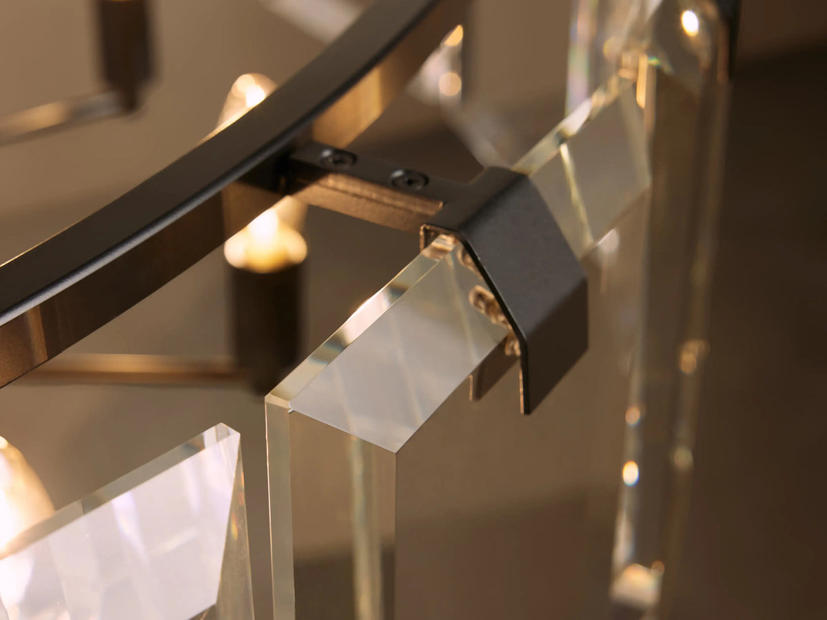 A close-up of a modern chandelier featuring clear, angular glass panels attached to a metal frame with a soft warm glow in the background.