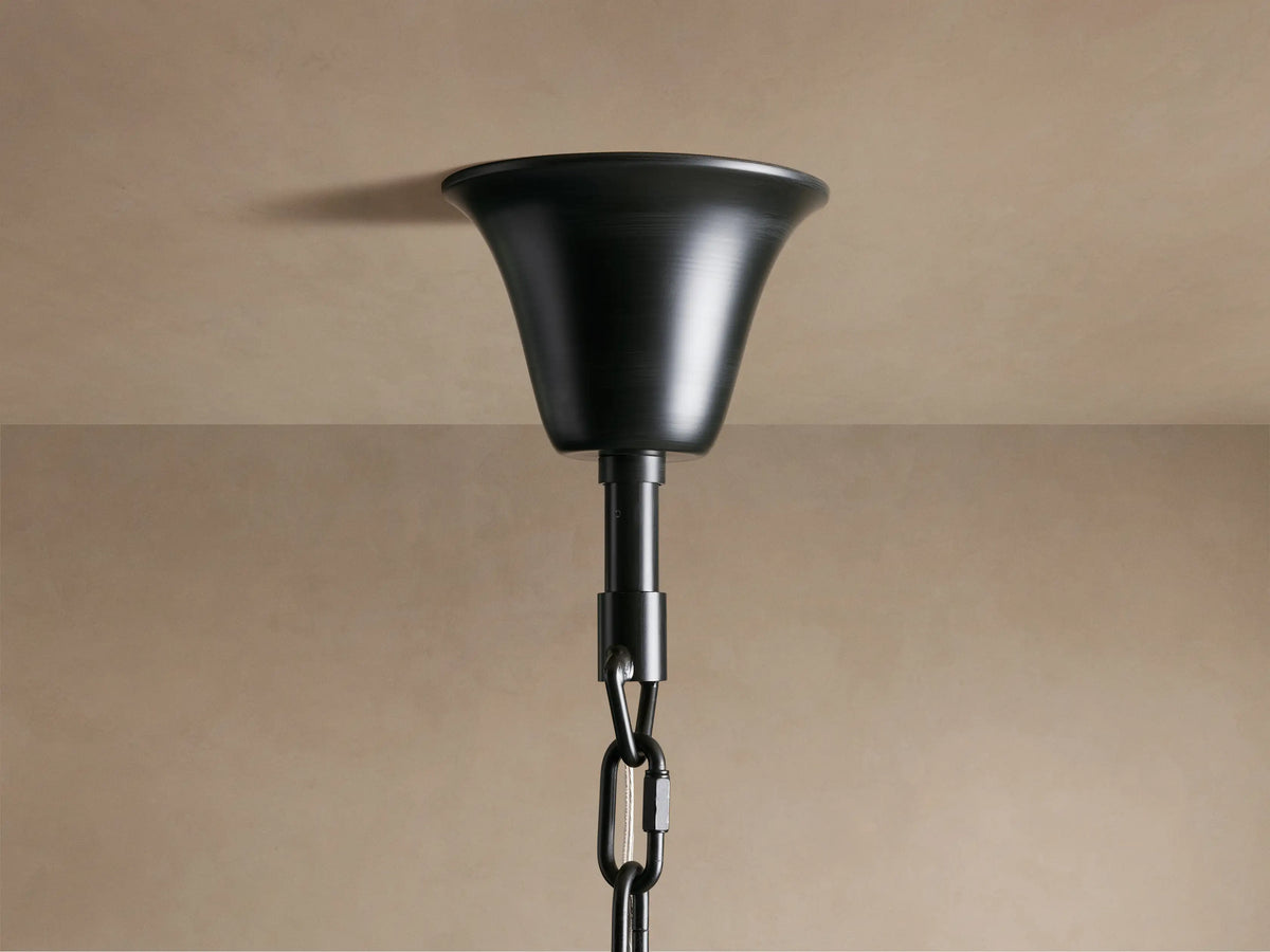 A close-up of a black metal ceiling fixture with a chain attachment against a beige ceiling and wall background.