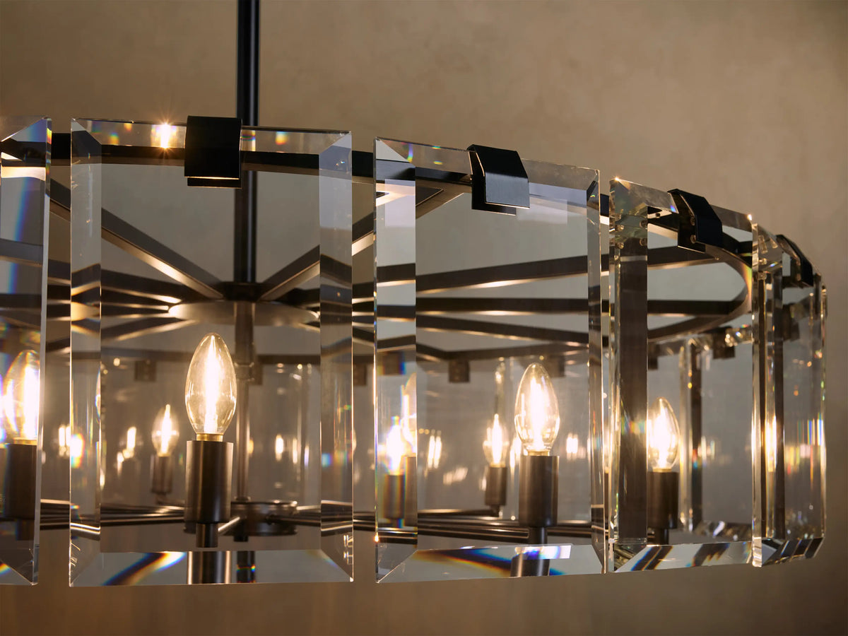 A rectangular chandelier with black metal frame features multiple candle-like bulbs surrounded by clear, faceted crystal panels emitting warm light.