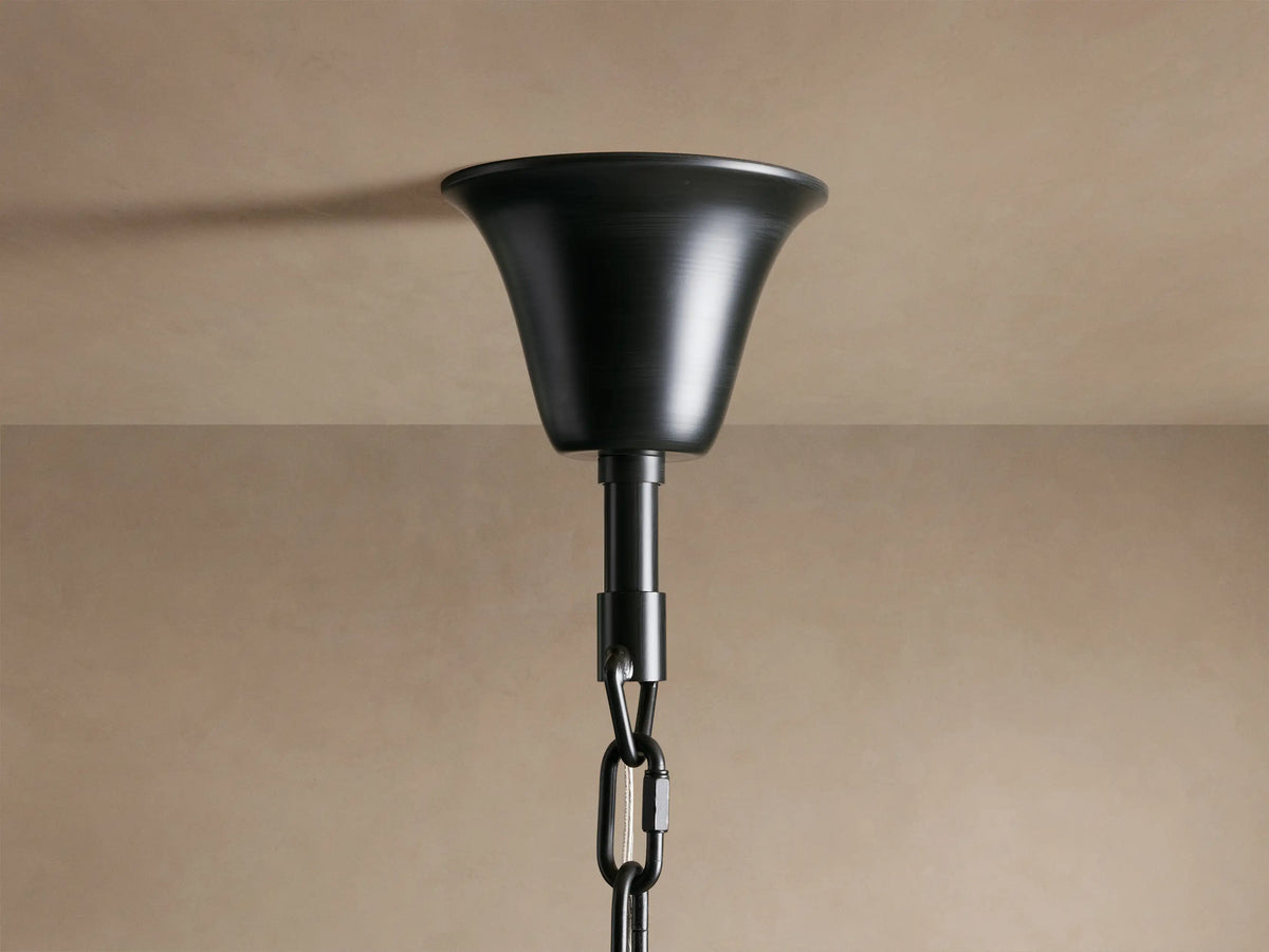 A black metal ceiling mount with a bell-shaped canopy and a link chain extends downward against a beige background.