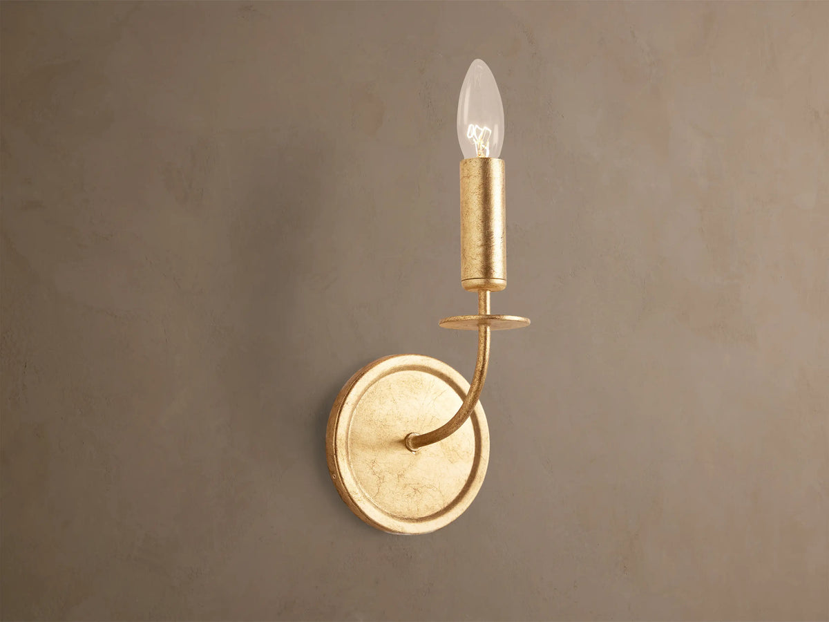 Arnett Sconce: antiqued gold leaf iron sconce with round backplate, curved arm, and candle-style holder with clear bulb.