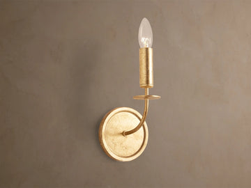 Arnett Sconce: antiqued gold leaf iron sconce with round backplate, curved arm, and candle-style holder with clear bulb.