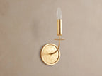 Arnett Sconce: antiqued gold leaf iron sconce with round backplate, curved arm, and candle-style holder with clear bulb.