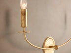 Arnett Double Sconce: antiqued gold iron wall light with two curved arms holding candlestick-style clear bulbs on a textured wall.