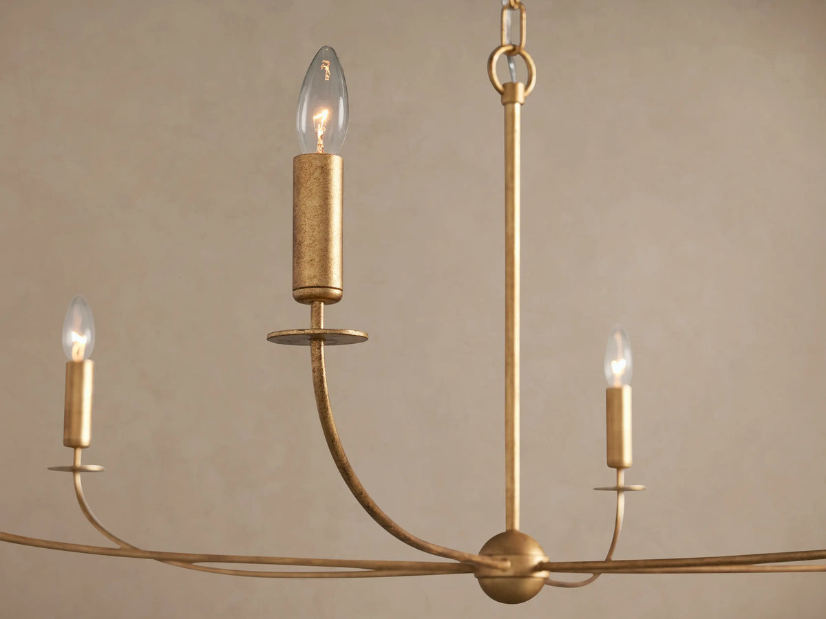Close-up of Arnett Chandelier with antiqued gold leaf finish, showing lit candle-style bulbs on curved arms.