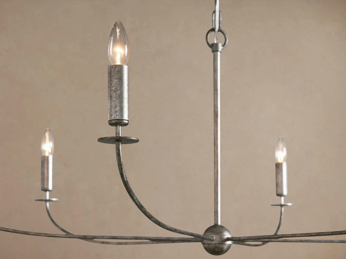 Arnett Round Chandelier with antiqued leaf finish, six candle-style lights, hanging by a chain against a beige wall.