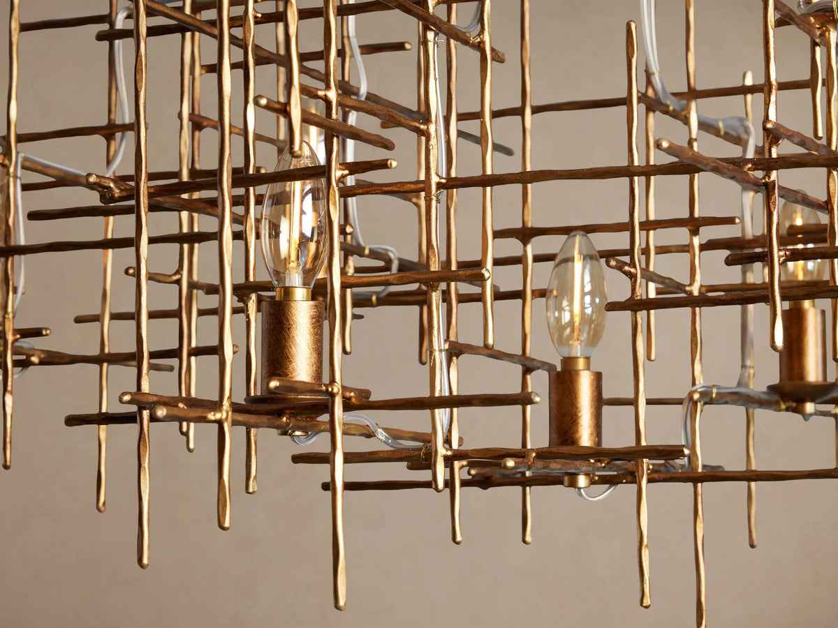 Fritz Chandelier: gold hand-hammered iron with an abstract grid design, featuring 7 exposed clear candle-style bulbs.