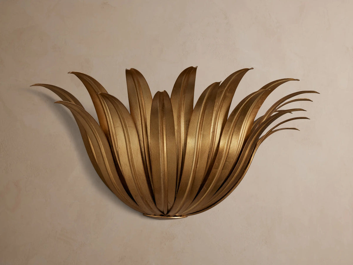 Matilde Sconce, an antique-gold iron wall light fixture with fanned, layered leaves, mounted on a light beige wall.