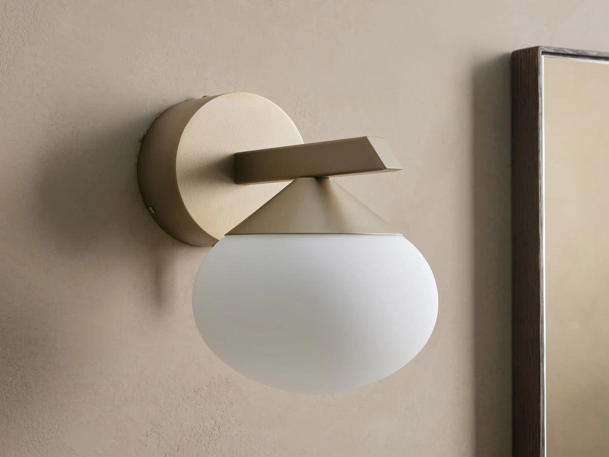 Costella Sconce: champagne/gold iron base, angled arm, and illuminated spherical opal glass diffuser mounted on a wall.