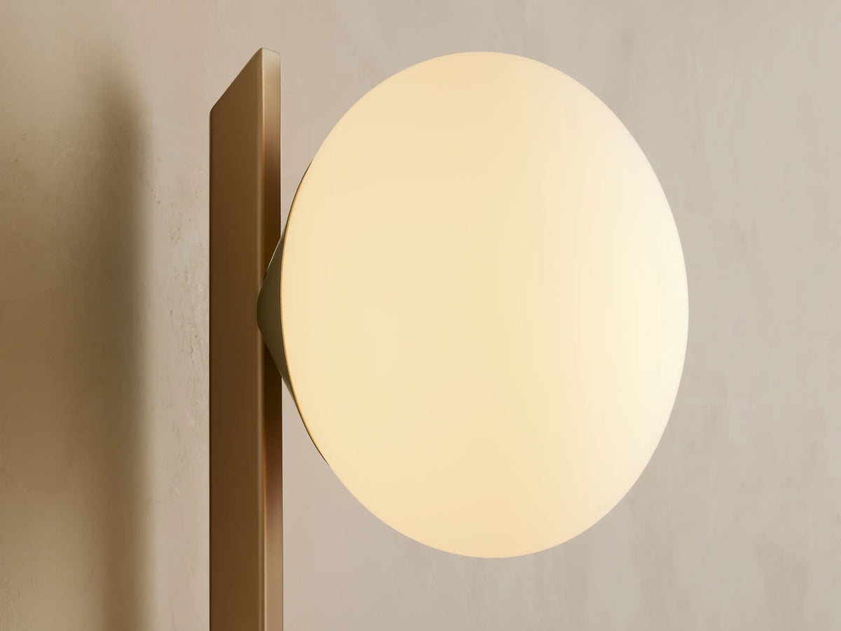 Costella Grand Sconce: Vertical champagne gold sconce with a spherical white opal glass diffuser, mounted on a light wall.