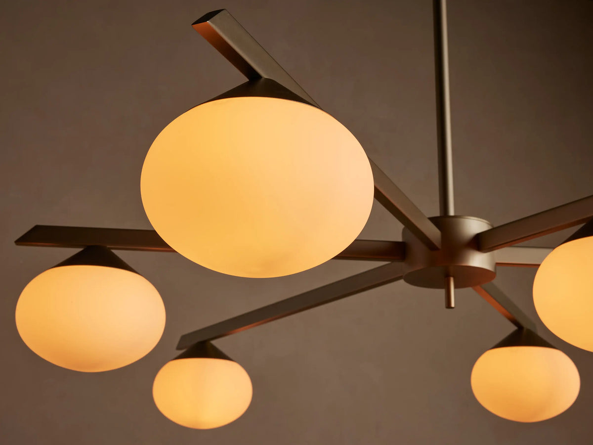 Costella Round Chandelier: Dark metallic frame with six glowing, round opal glass diffusers emitting warm light.