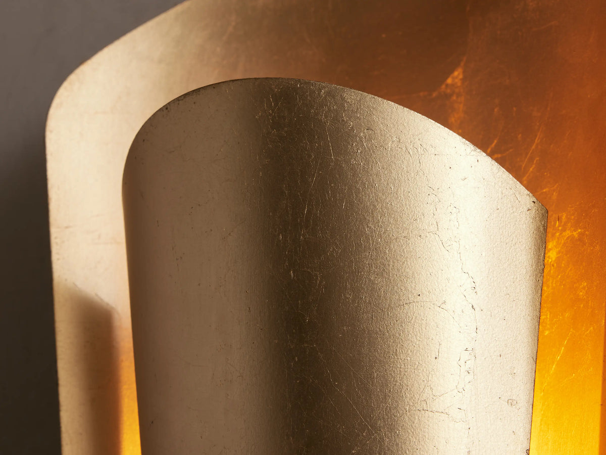Strato Sconce, a vertical, curved gold brass wall sconce with a hand-applied leafed finish, mounted on a neutral wall.
