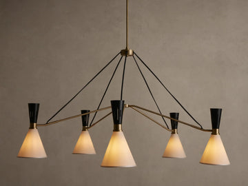 Ramsey Round Chandelier with five glowing white fabric conical shades, black accents, and brass arms on a beige wall.