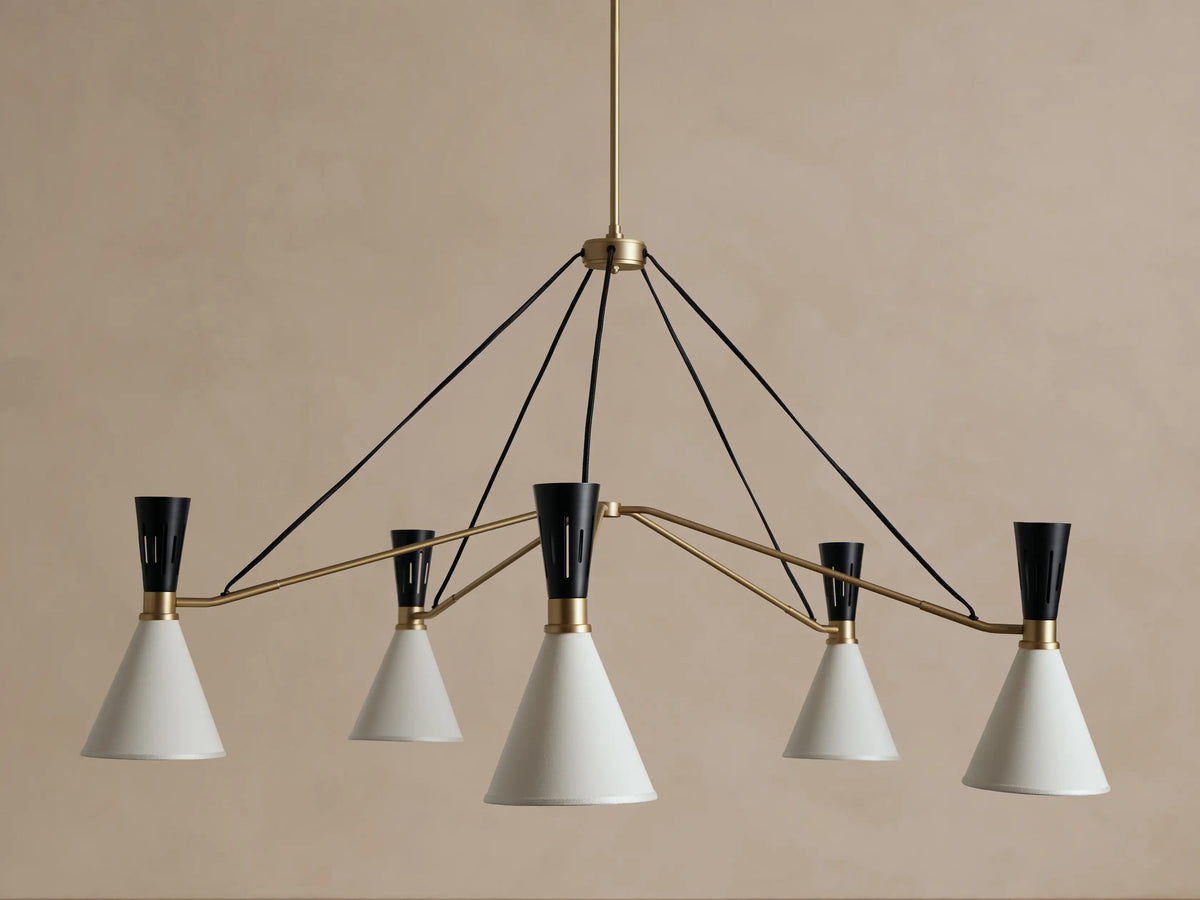 Ramsey Round Chandelier with five glowing white fabric conical shades, black accents, and brass arms on a beige wall.