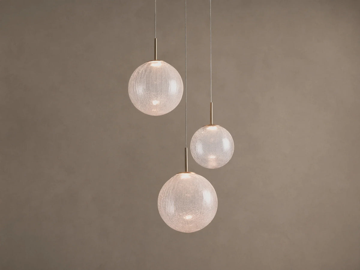 Casen Round Chandelier. Three illuminated crackle glass globes with satin brass accents, suspended at varying heights.