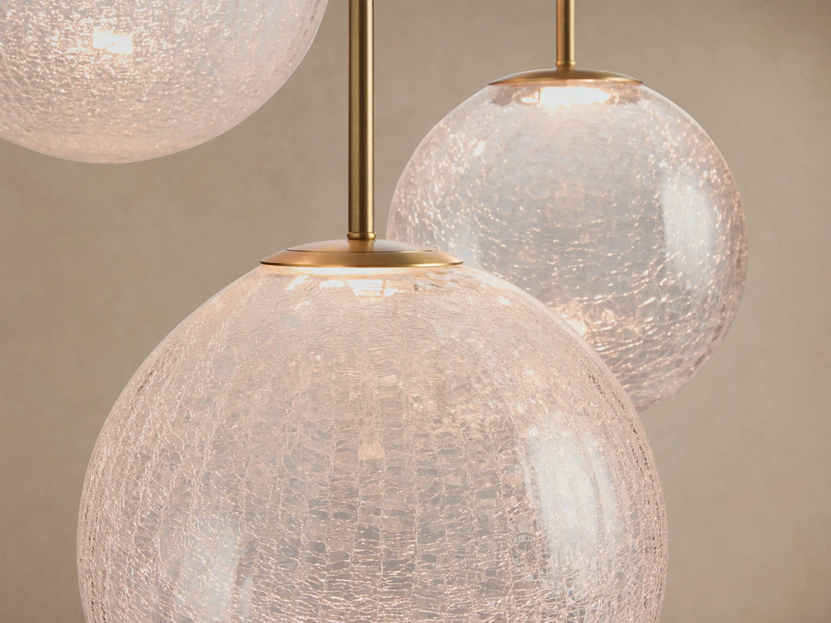 Close-up of Casen Round Chandelier with multiple illuminated crackle glass globes and satin brass rods against a light background.