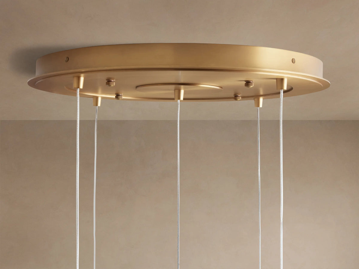 Close-up of Casen Round Chandelier's satin brass ceiling mount, with several thin white suspension cables descending.