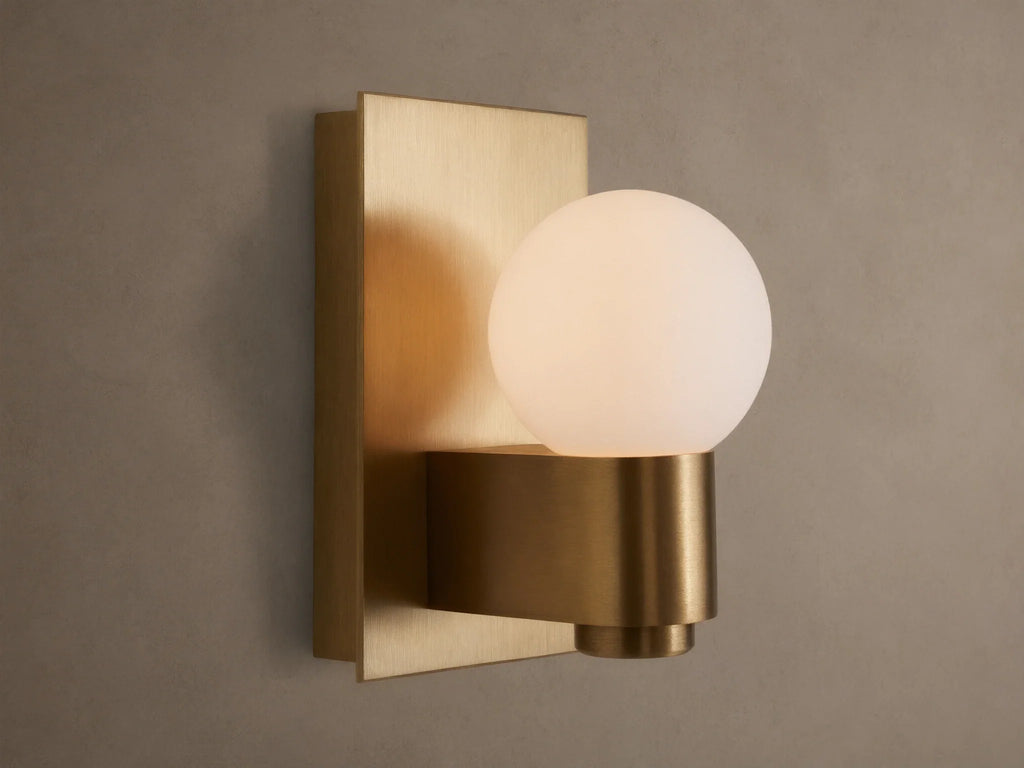 Illuminated Casen Sconce with a glowing mouth-blown solid opal glass globe on a satin brass fixture.