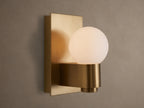 Illuminated Casen Sconce with a glowing mouth-blown solid opal glass globe on a satin brass fixture.