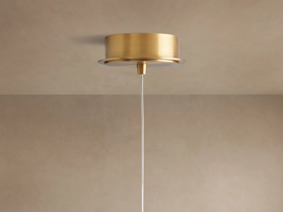 Close-up of Casen Pendant showing a glowing white opal glass globe with a satin brass stem and cap against a light wall.
