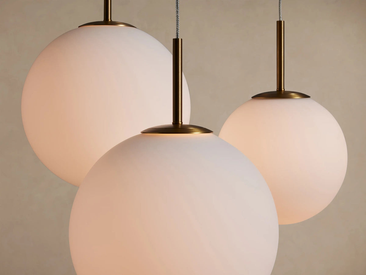 Casen Round Chandelier with three glowing spherical opal glass globes hanging from satin brass rods against a light background.