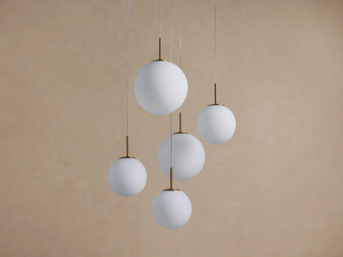 Casen Round Chandelier with five white opal glass globes and satin brass accents, hanging in a staggered arrangement.