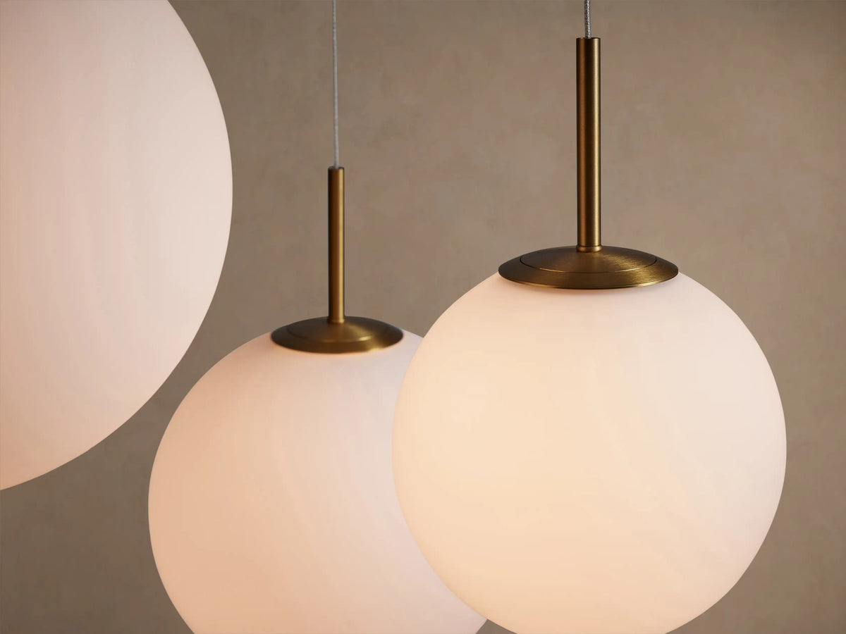 Casen Round Chandelier. Close-up of two illuminated white opal glass globes hanging from satin brass hardware.