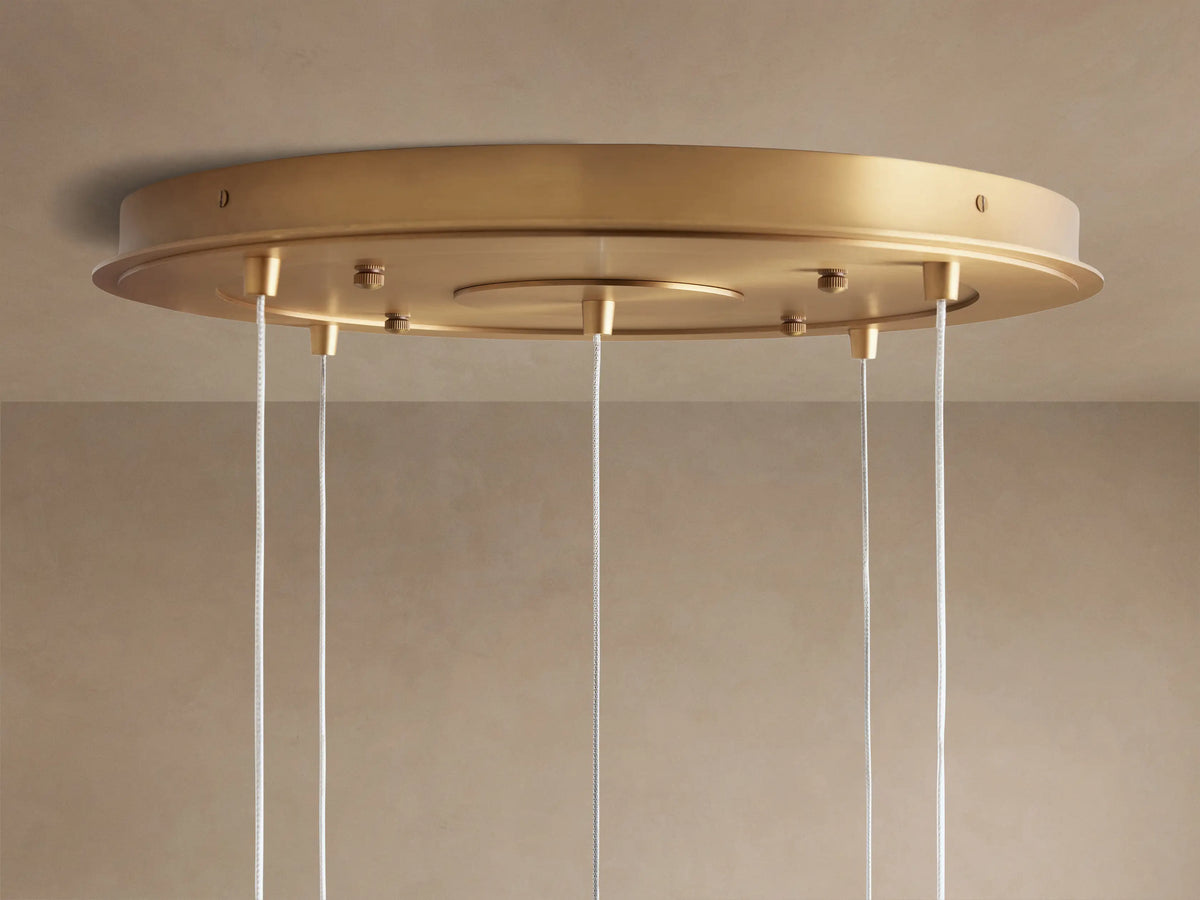 Casen Round Chandelier's circular satin brass ceiling mount, seen from below, with several white wires hanging.