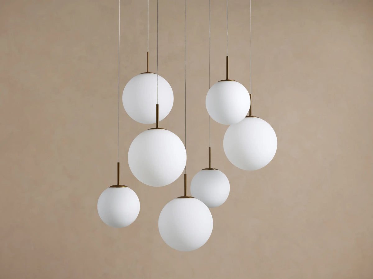Casen Round Chandelier with seven white opal glass globes suspended at different heights by thin wires and brass rods.