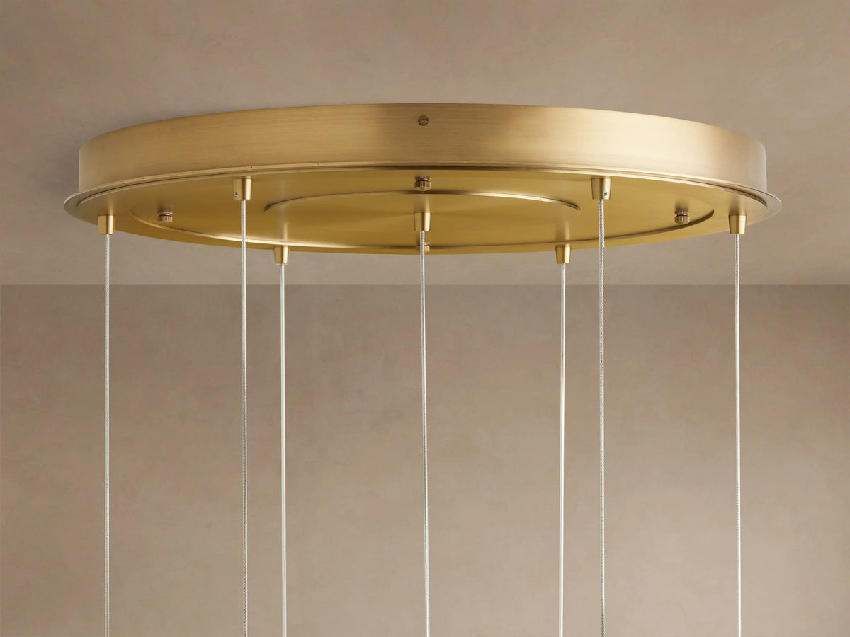 Close-up of Casen Round Chandelier's satin brass ceiling canopy with many thin white hanging cables against a beige ceiling.