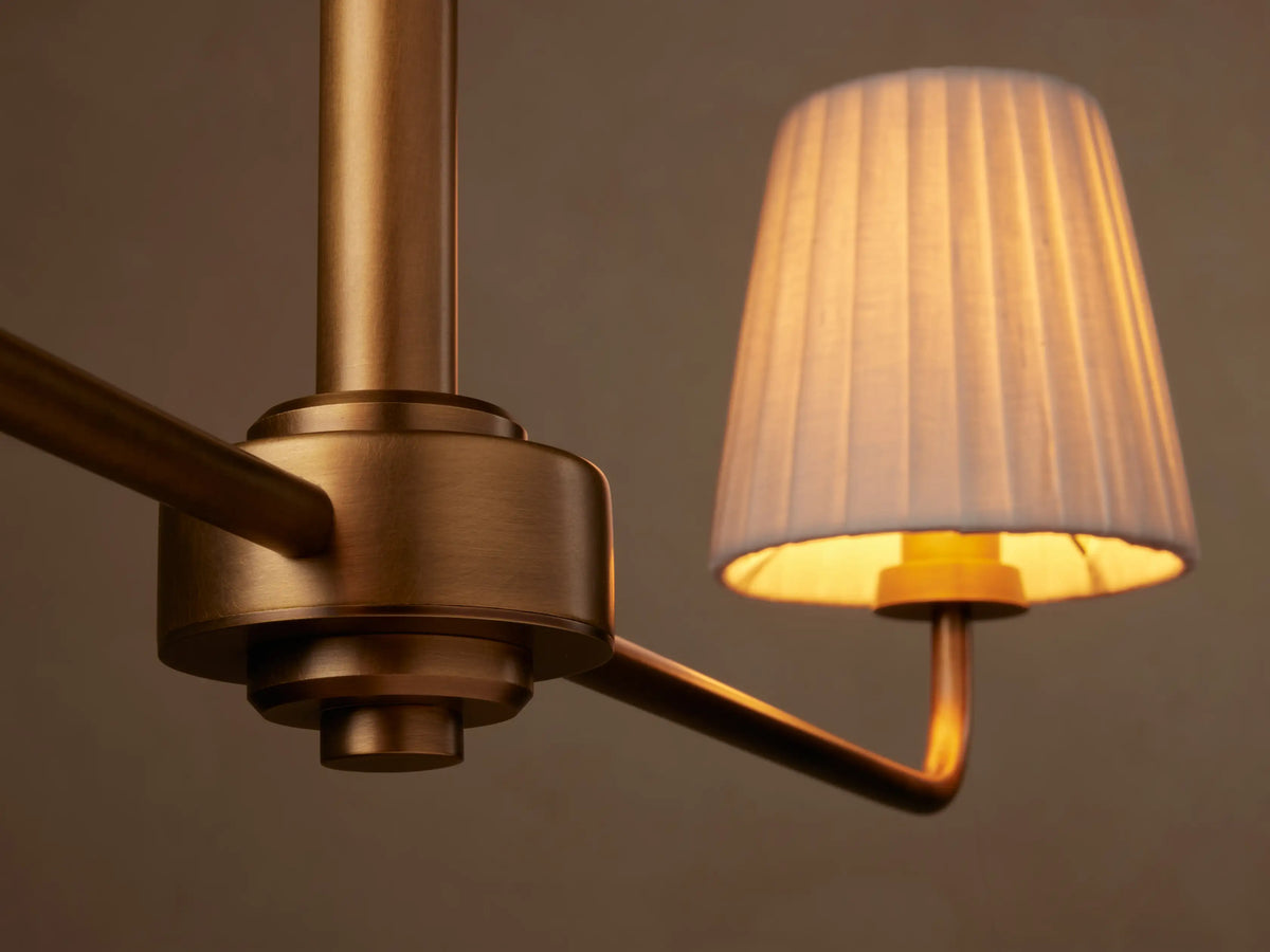 Adria 2-Light Chandelier: brass-toned iron hanging fixture with a horizontal bar and two white pleated shades on a beige wall.