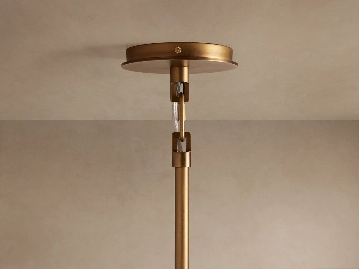 Close-up of the Adria 2-Light Chandelier, showing its brushed brass arm and illuminated pleated white shade with a warm glow.