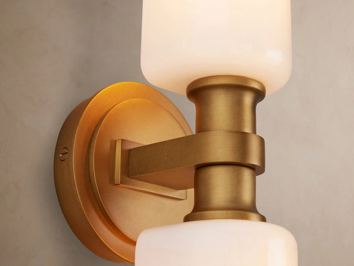 Zayd Double Sconce with two elongated white glass shades and a brass-finished metal mount, oriented vertically on a wall.