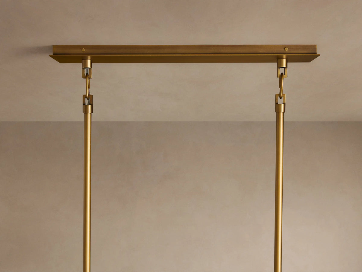 Close-up of Adria Linear Chandelier. Brass frame supports four glowing, light-colored fabric shades with matching brass trim.