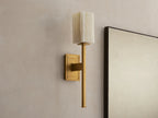 Cinda Sconce: Wall-mounted brass sconce with an illuminated rectangular natural stone shade next to a mirror on a beige wall.