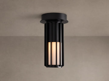 Matte black Gabbia Outdoor Spotlight Flush Mount, cylindrical with vertical slats, flush-mounted to a light brown ceiling. Inner milk glass panels glow.