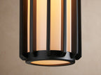 Matte black Gabbia Outdoor Sconce with a rectangular backplate, cylindrical ribbed body, and white milk glass, on a beige wall.