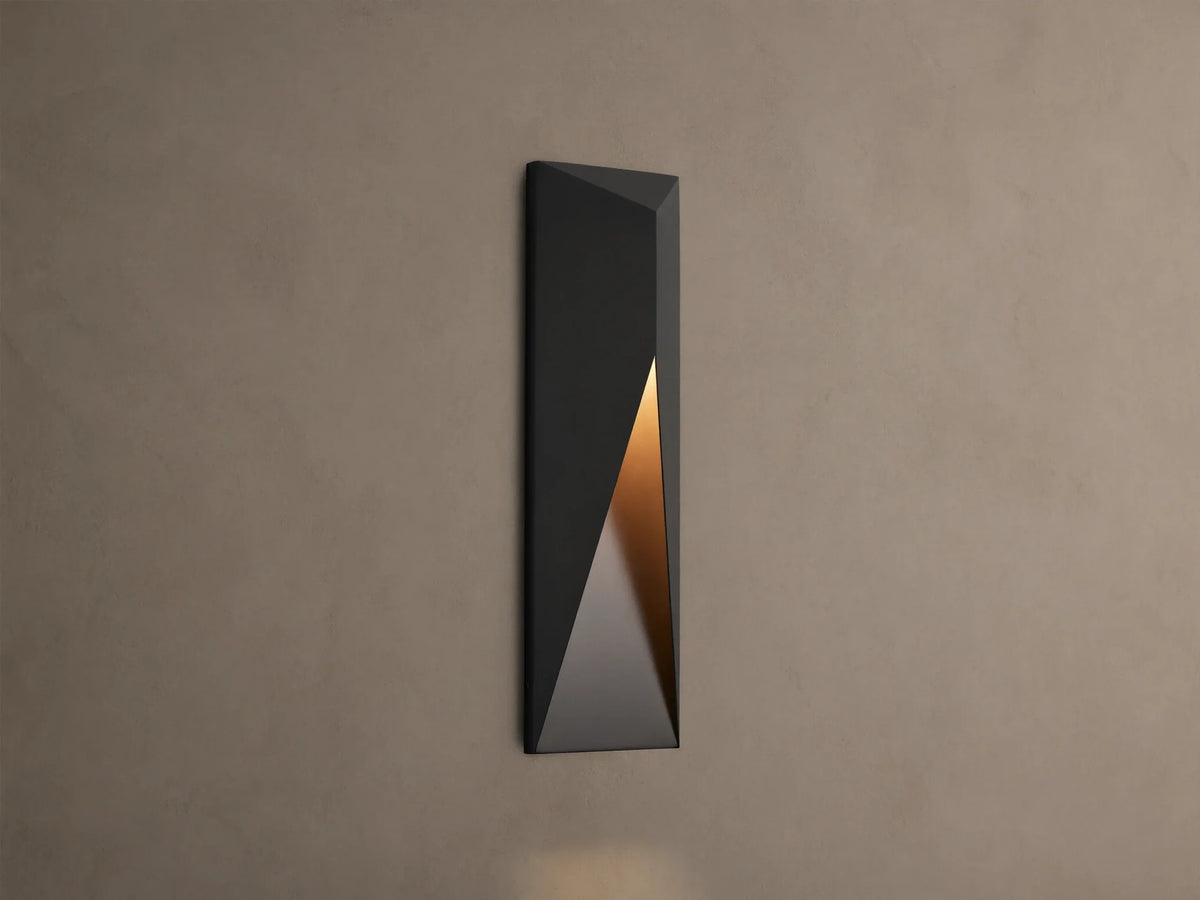 Modern dark grey Davian Outdoor Sconce, vertically mounted, with geometric facets and warm bronze light emanating from inside.