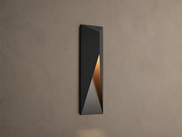 Modern dark grey Davian Outdoor Sconce, vertically mounted, with geometric facets and warm bronze light emanating from inside.