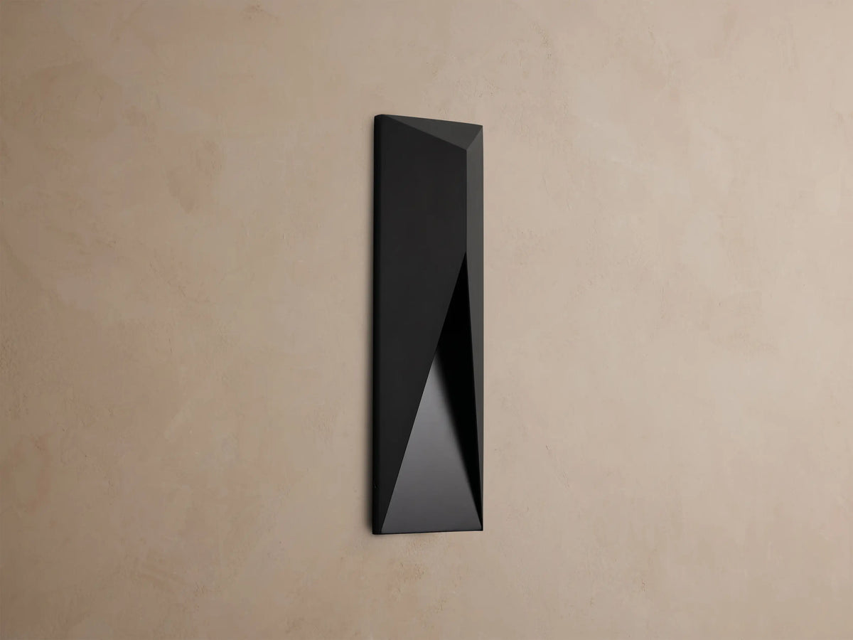 Modern dark grey Davian Outdoor Sconce, vertically mounted, with geometric facets and warm bronze light emanating from inside.