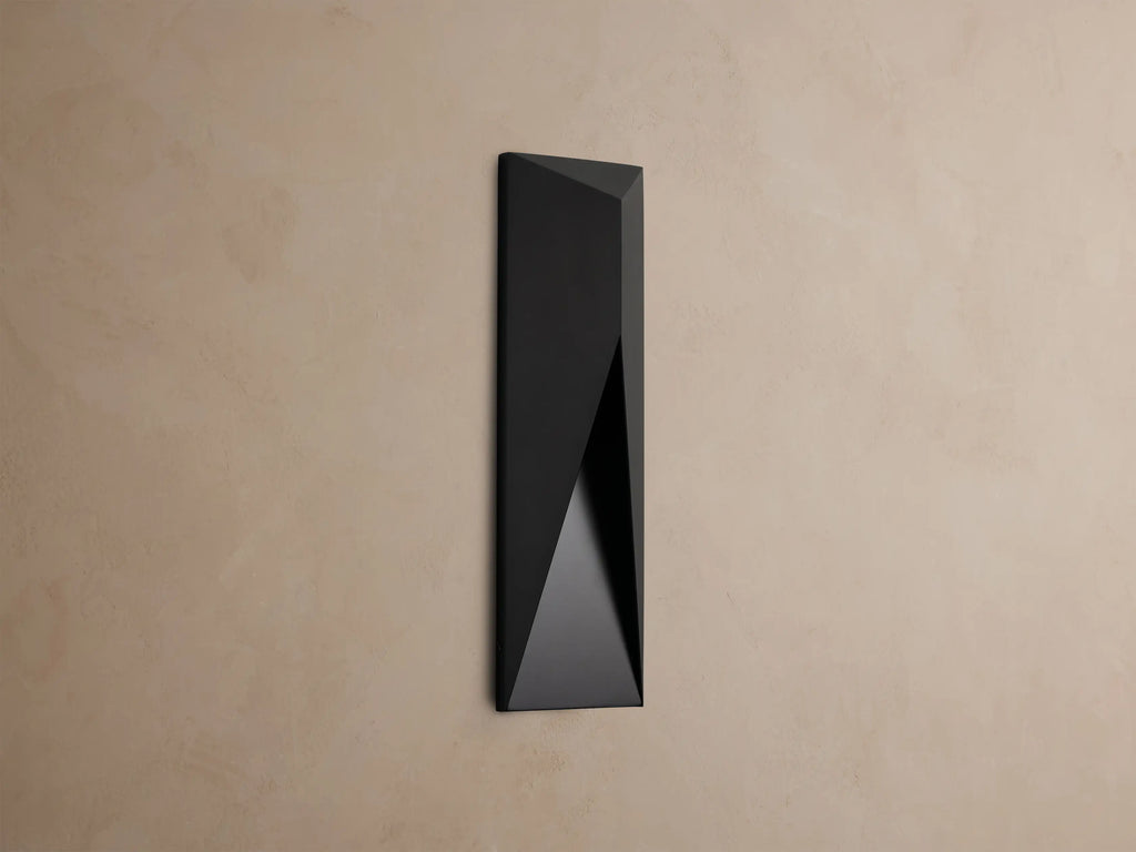 Modern dark grey Davian Outdoor Sconce, vertically mounted, with geometric facets and warm bronze light emanating from inside.